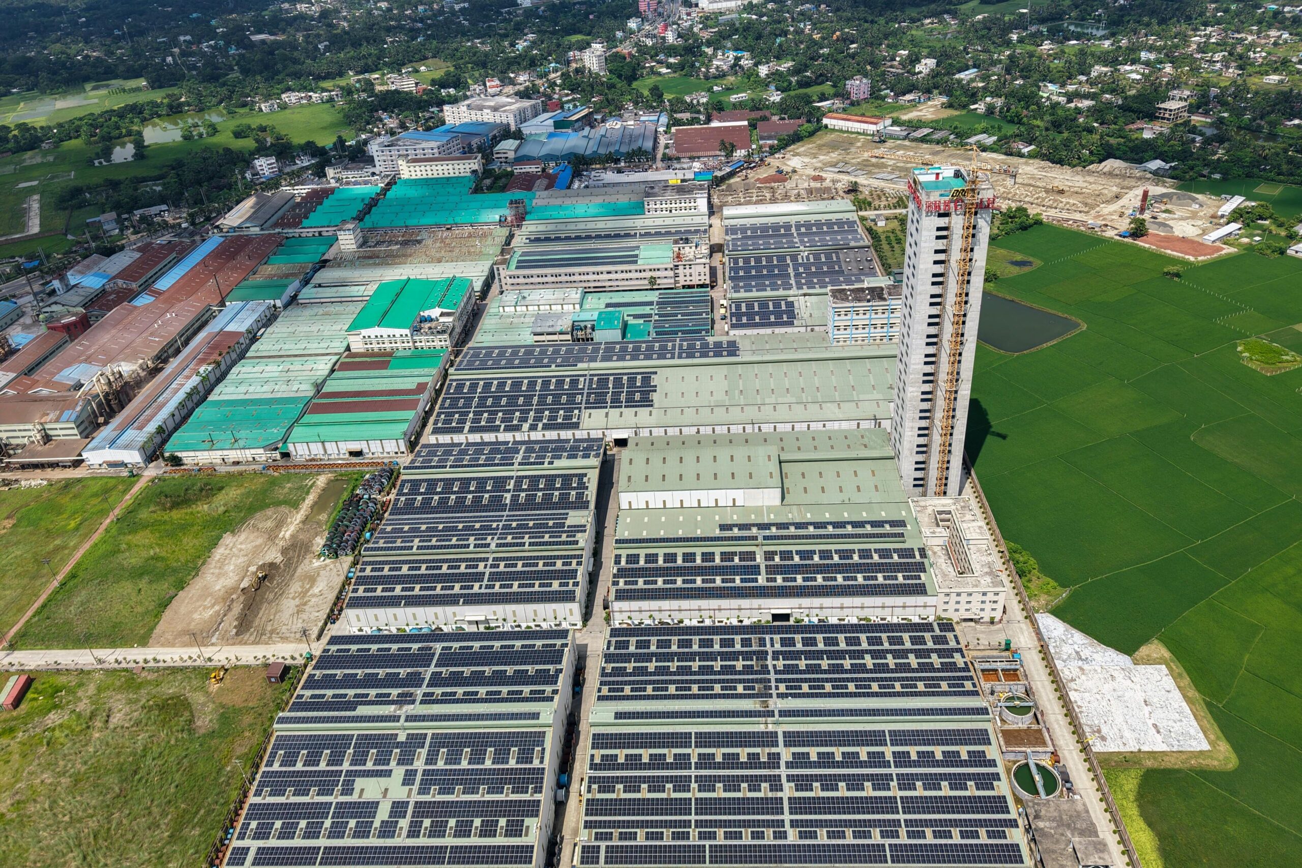 Sprawling industrial complex with solar panels and green fields, seen from above.